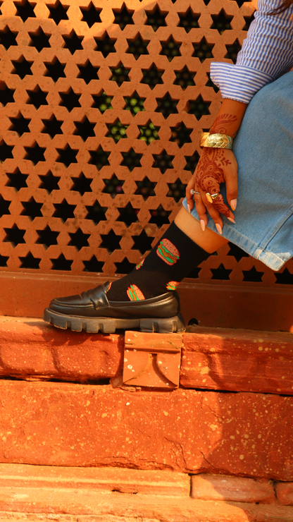 Model wearing Saucy Burger funky socks – black ankel-length cotton socks with fun burger print for food lovers.